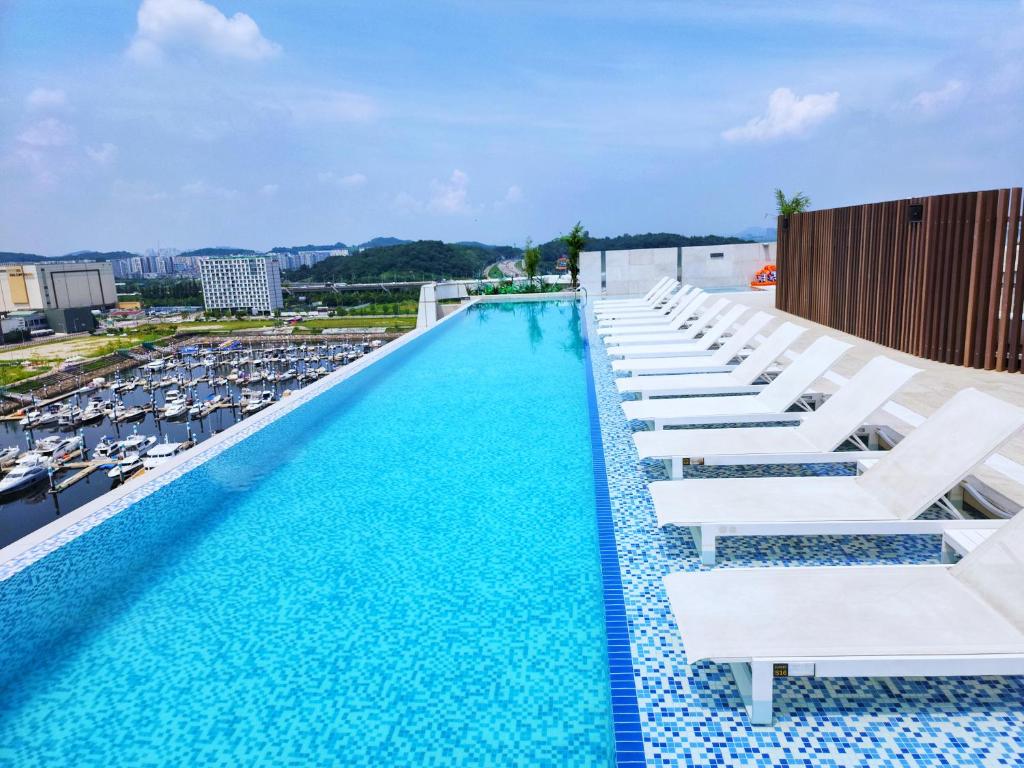 a large swimming pool with white lounge chairs and boats at Hotel Marinabay Seoul Ara in Gimpo