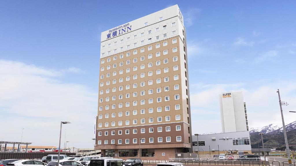 een hoog gebouw met auto's geparkeerd op een parkeerplaats bij Toyoko Inn Joetsu myoko eki Nishi guchi in Joetsu