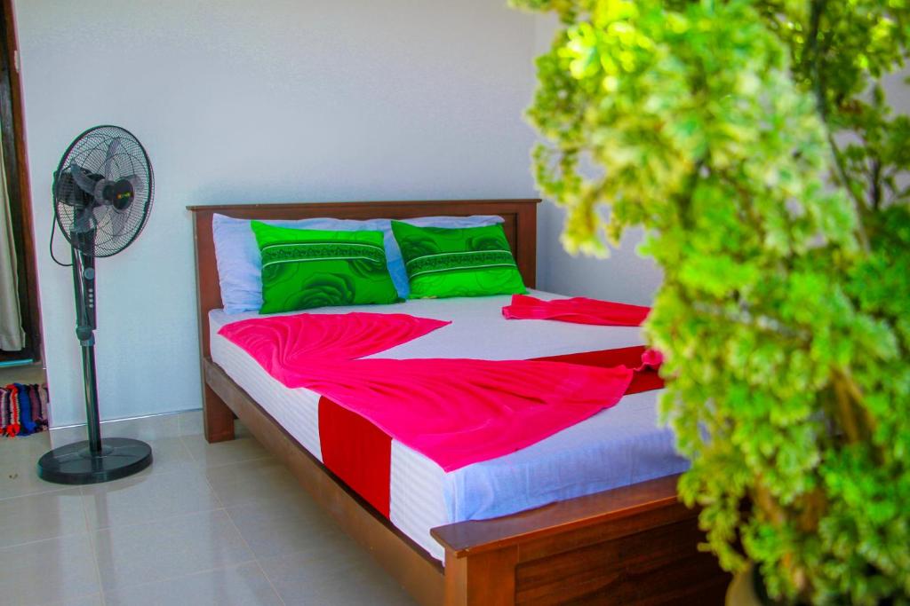 Cette chambre comprend un lit avec des draps verts et rouges ainsi qu'un ventilateur. dans l'établissement Keth Sisila Villa, à Dambulla