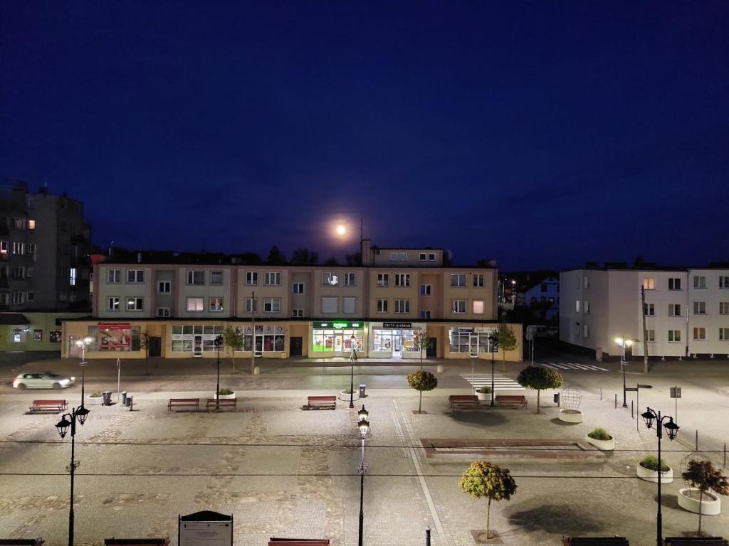 a parking lot with benches and buildings at night at Apartament przy Rynku in Olsztynek