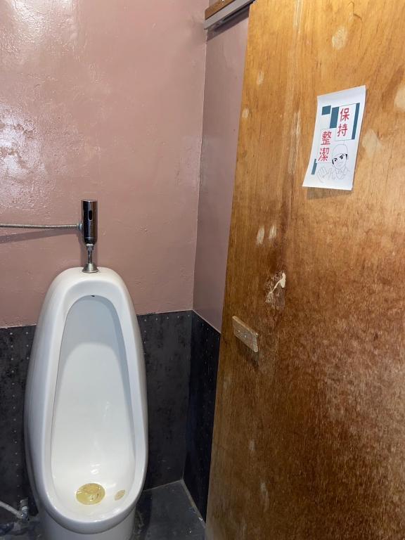 a bathroom stall with a urinal and a wooden door at Hive Bed and Backpacker蜂巢膠囊旅店 in Hualien City