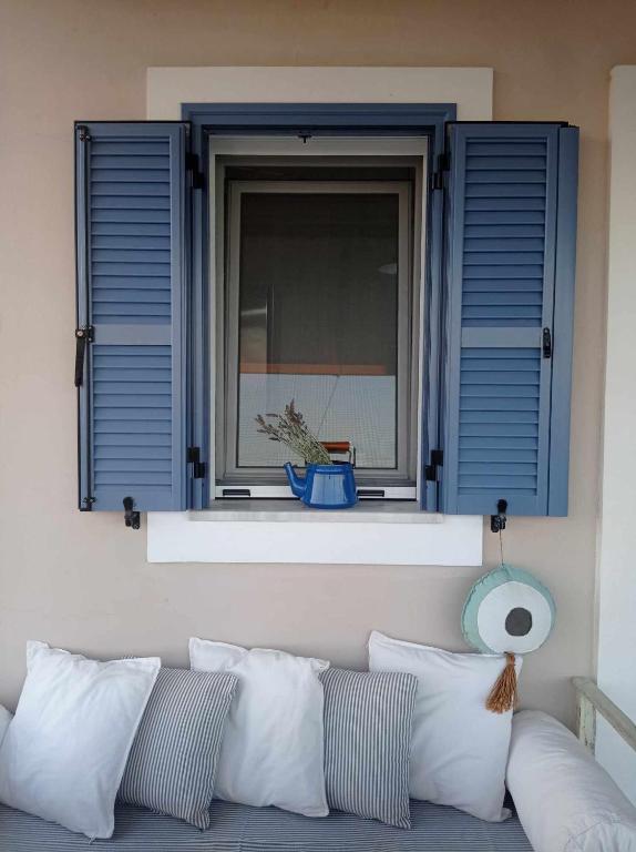 a window with blue shutters and a couch with pillows at Seaside resort- kallithea in Kallithéa