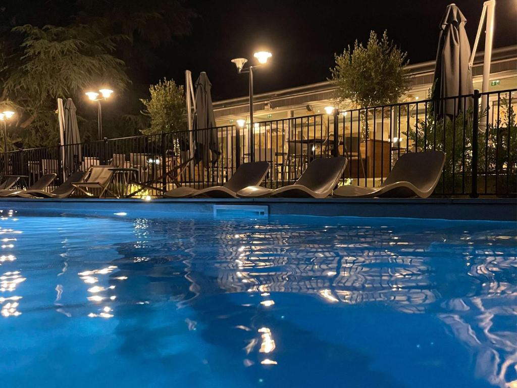 una piscina por la noche con sillas y sombrillas en Novotel Pau Pyrénées, en Lescar