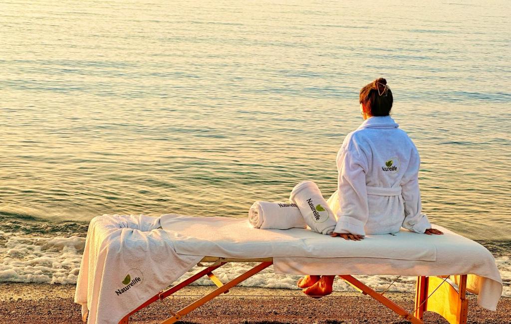 a woman sitting on a bench on the beach at Naturelife Bungalows & SPA in Cıralı