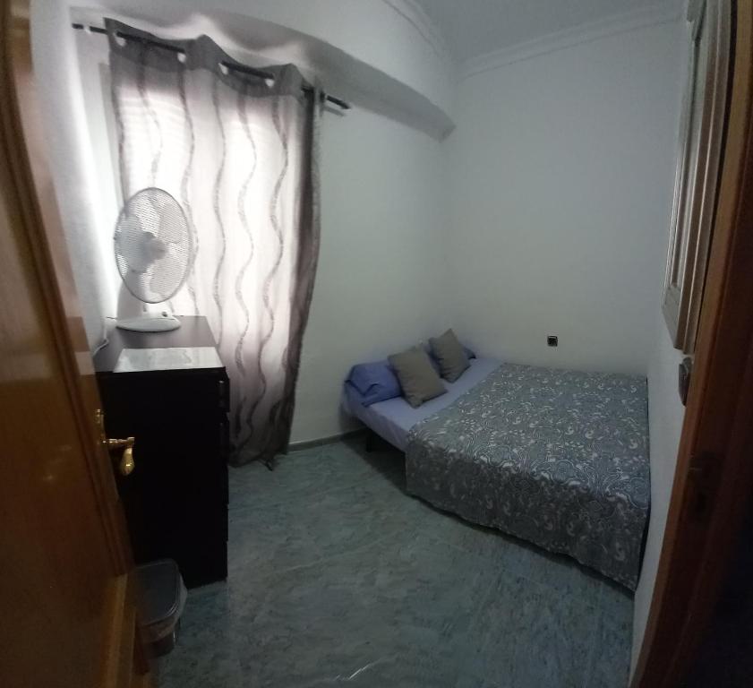 um pequeno quarto com uma cama e uma ventoinha em habitación pequeña en piso compartido con 2 adultos y 1 perrito em Valência