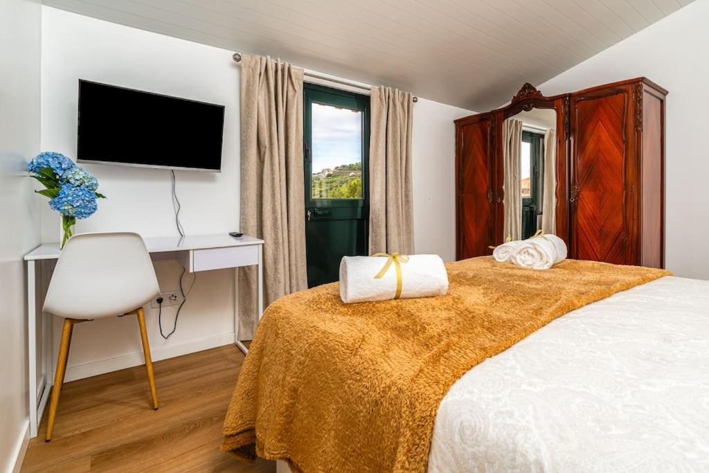 a bedroom with a bed with a television and a chair at Fénix House in Arco da Calheta