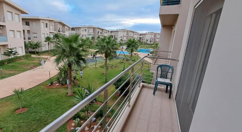 Un balcón con una silla azul y vista a un parque. en Appartement Plage Mehdia - Residence Kenz Mehdya Beach, en Kenitra