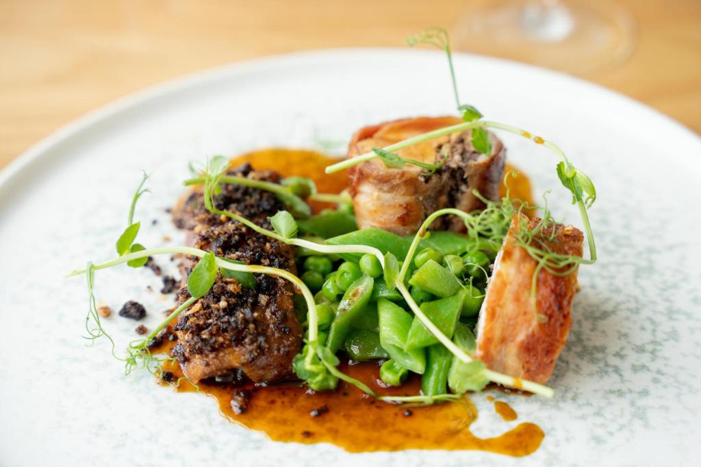 a plate of food with meat and greens on it at Fistral Beach Hotel and Spa - Adults Only in Newquay