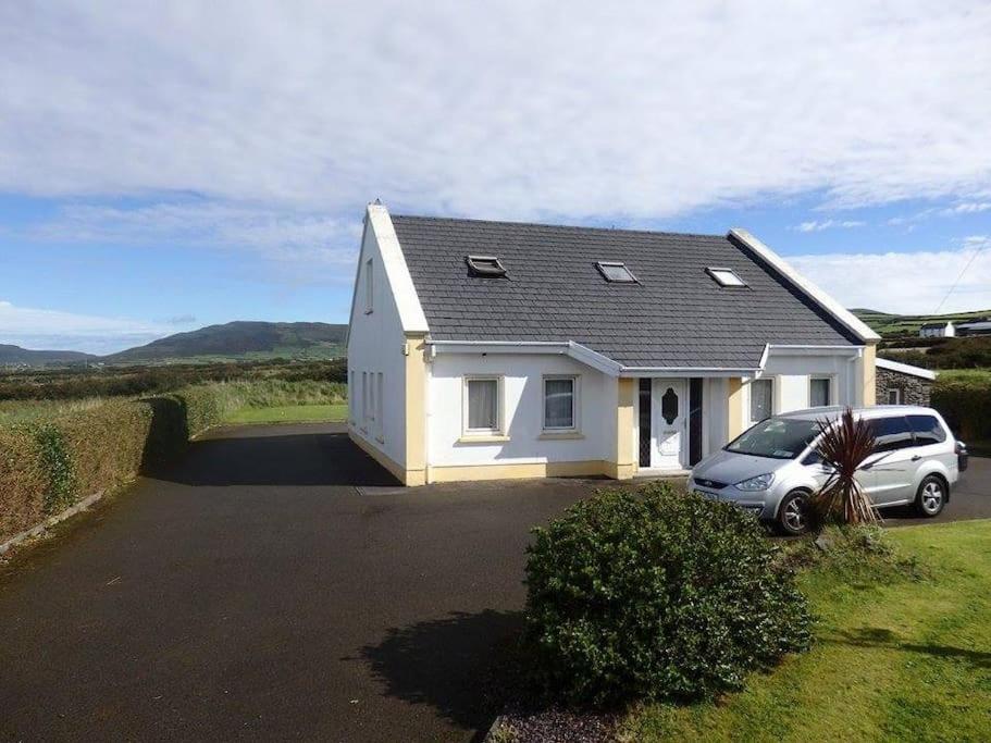 a white house with a car parked in a driveway at Three Sisters Holiday Home - 7km to Dingle in Ballyferriter