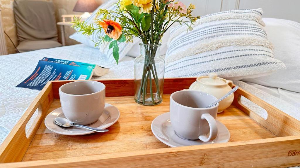 a tray with two cups and a vase with flowers on a bed at La Maison des Hautures in Arles