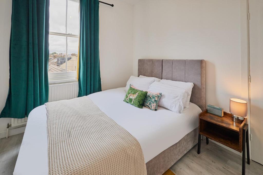 een slaapkamer met een wit bed, groene gordijnen en een raam bij Host & Stay - Cosy Twickenham Rugby Gem in Twickenham