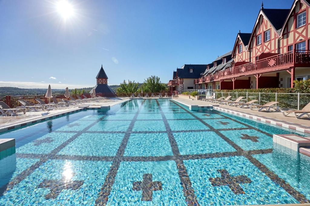 a large swimming pool with chairs and a building at Pierre & Vacances Premium Residence & Spa Houlgate in Houlgate