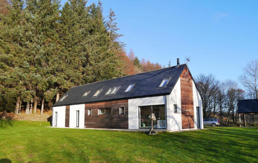 een witte schuur met een zwart dak op een groen veld bij Laundry Cottage in Aberlour