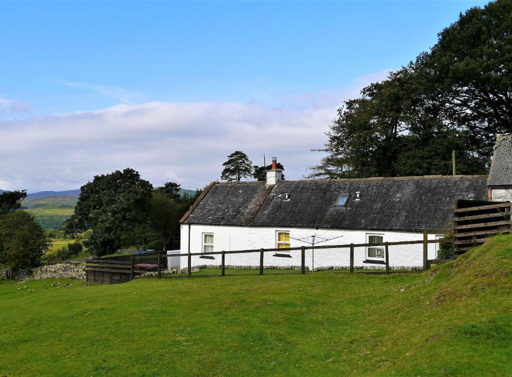 a white house with a black roof on a green field at Laghead Steading Cottage in Gatehouse of Fleet