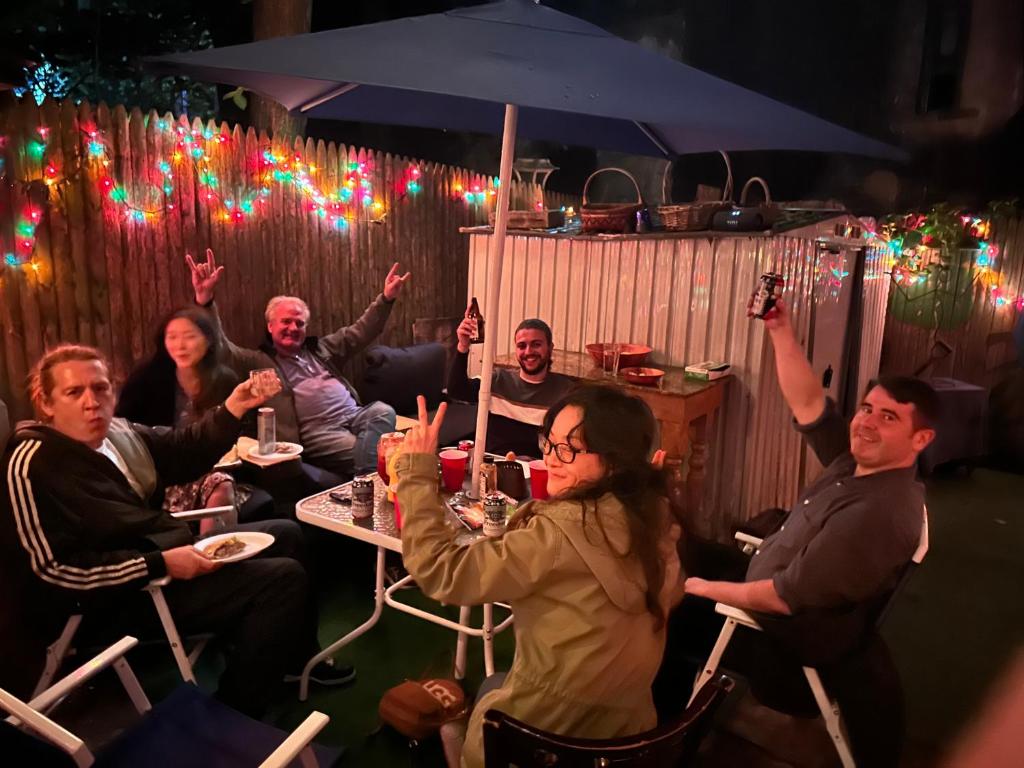 a group of people sitting at a table with their hands up at Macaw Guest House in New York