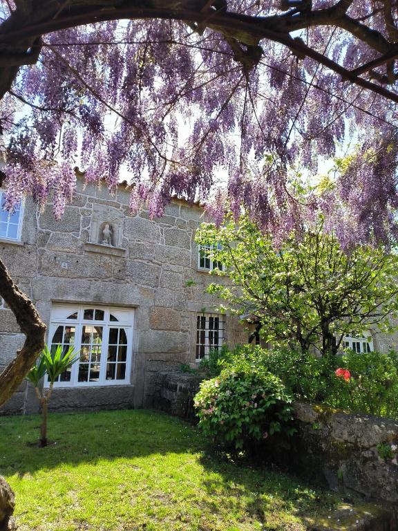 a stone house with a tree with purple flowers at CASA DO ARCO - BARCELOS in Barcelos