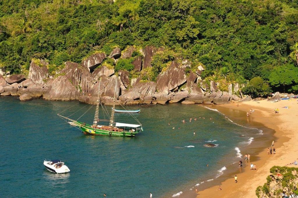 a green boat in the water next to a beach at Chalés da Barra Ilhabela in Ilhabela