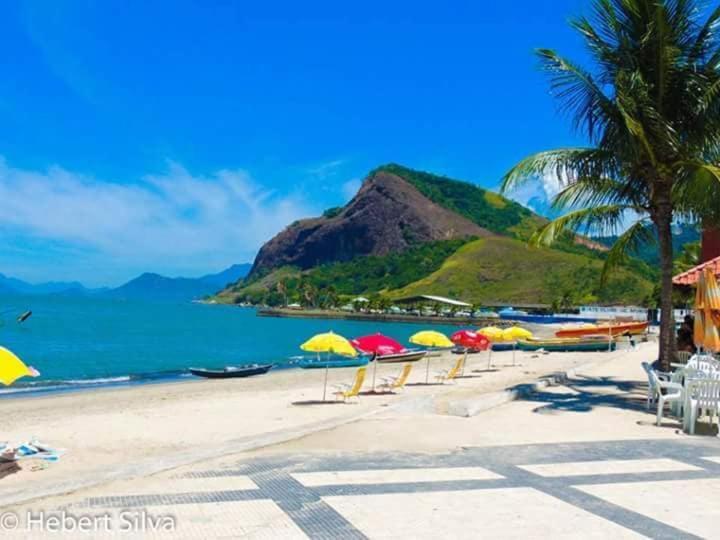ein Strand mit Sonnenschirmen und Stühlen und das Meer in der Unterkunft Cantinho feliz de Muriqui/ Casa verde com piscina privativa!!! in Mangaratiba