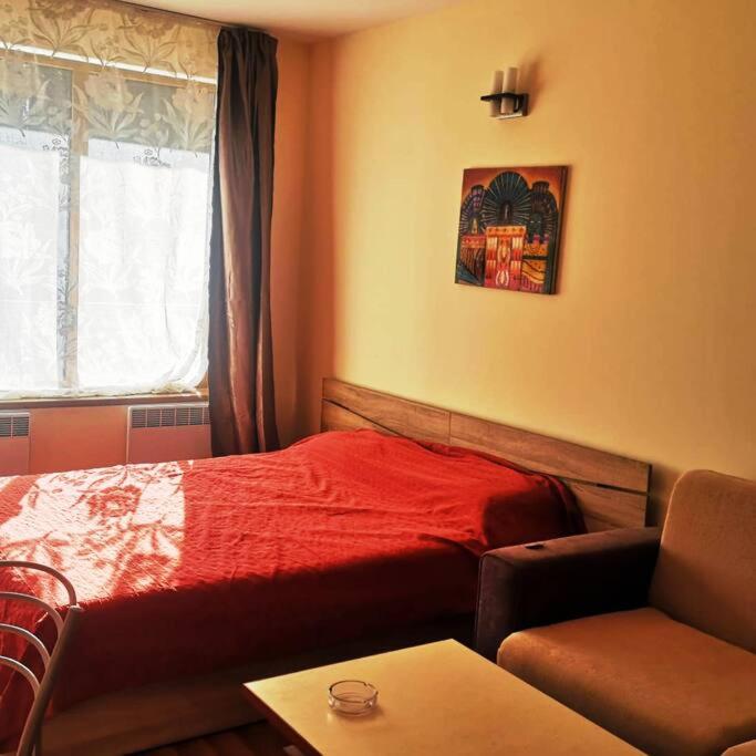 um quarto com uma cama vermelha, uma cadeira e uma mesa em Cozy sunny studio. em Pamporovo