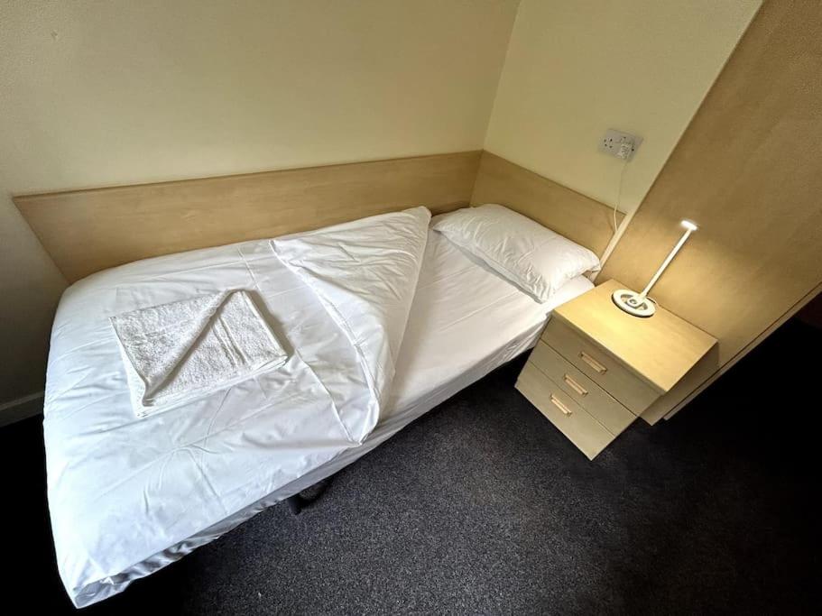ein Schlafzimmer mit einem Bett mit weißer Bettwäsche und einem Nachttisch in der Unterkunft Spacious Ensuite Room With Shared Kitchen and Living Room in Crewe