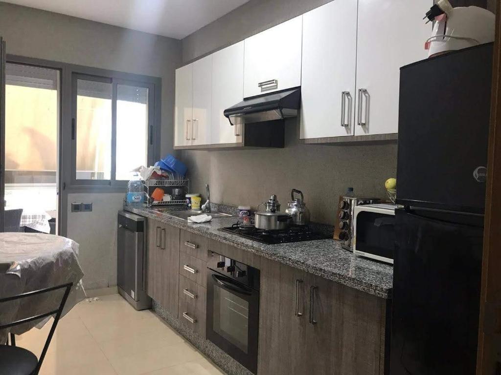 La cuisine est équipée de placards blancs et d'un réfrigérateur noir. dans l'établissement Bel Appartement pour vacances, à Sidi Rahal