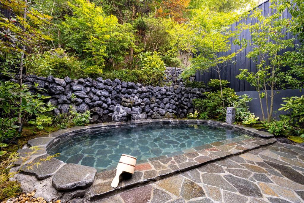 a small swimming pool in a garden with a stone wall at Bessho Onsen Midoriya in Ueda