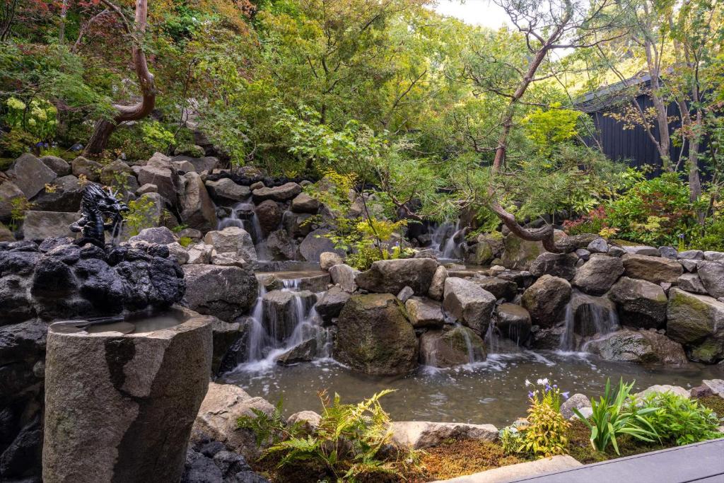 a waterfall in a garden with rocks and trees at Bessho Onsen Midoriya in Ueda
