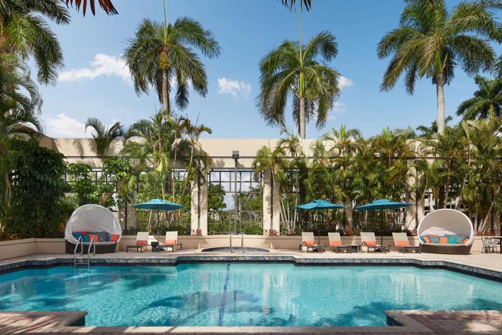 a pool with chairs and umbrellas and palm trees at Boca Raton Marriott at Boca Center in Boca Raton