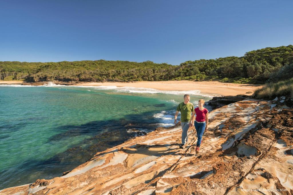 un hombre y una mujer caminando sobre las rocas cerca del océano en Joalah Holiday Park en Durras