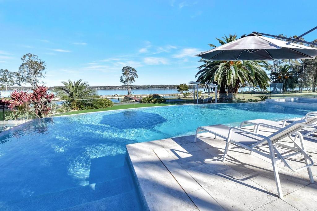 - une piscine avec 2 chaises et un parasol dans l'établissement Lake Palm Resort Luxury Retreat absolute Waterfront on 3 acres at Lake Macquarie., à Dora Creek
