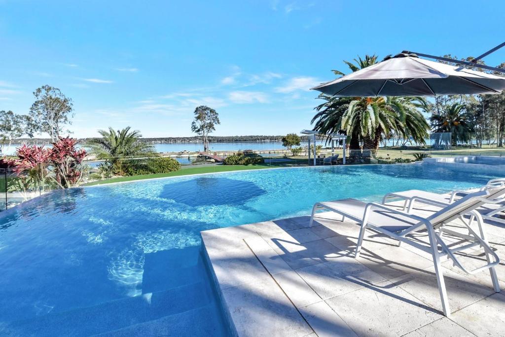 a swimming pool with two chairs and an umbrella at Lake Palm Resort Luxury Retreat absolute Waterfront on 3 acres at Lake Macquarie. in Dora Creek