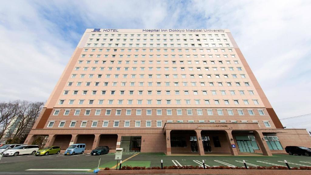 Un grand bâtiment avec des voitures garées devant lui dans l'établissement Toyoko Inn HOSPITAL INN Dokkyo Medical University, à Mibu