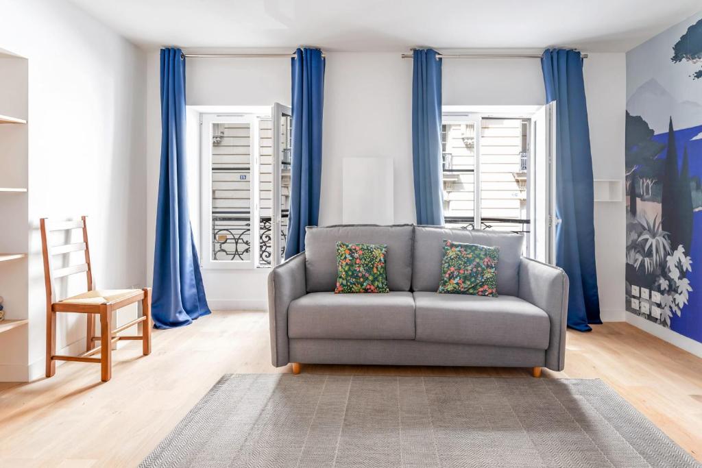 a living room with a gray couch and blue curtains at Renovated studio in the 6th district of Paris - Welkeys in Paris