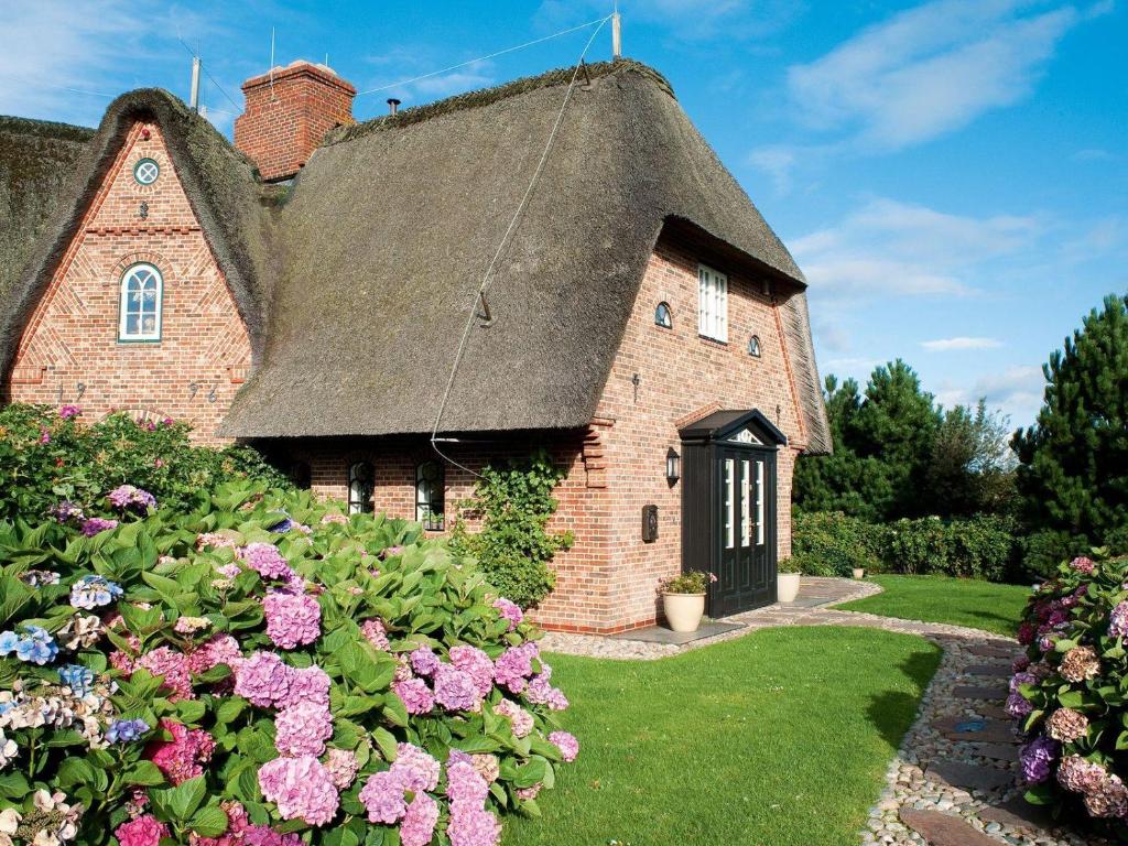 an old brick house with a thatched roof and flowers at Hortensienhues-Sued in Kampen
