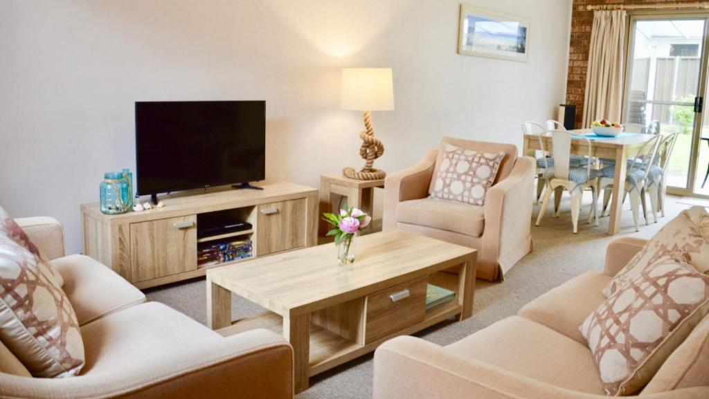 a living room with a tv and chairs and a table at Lighthouse Palms in Ulladulla