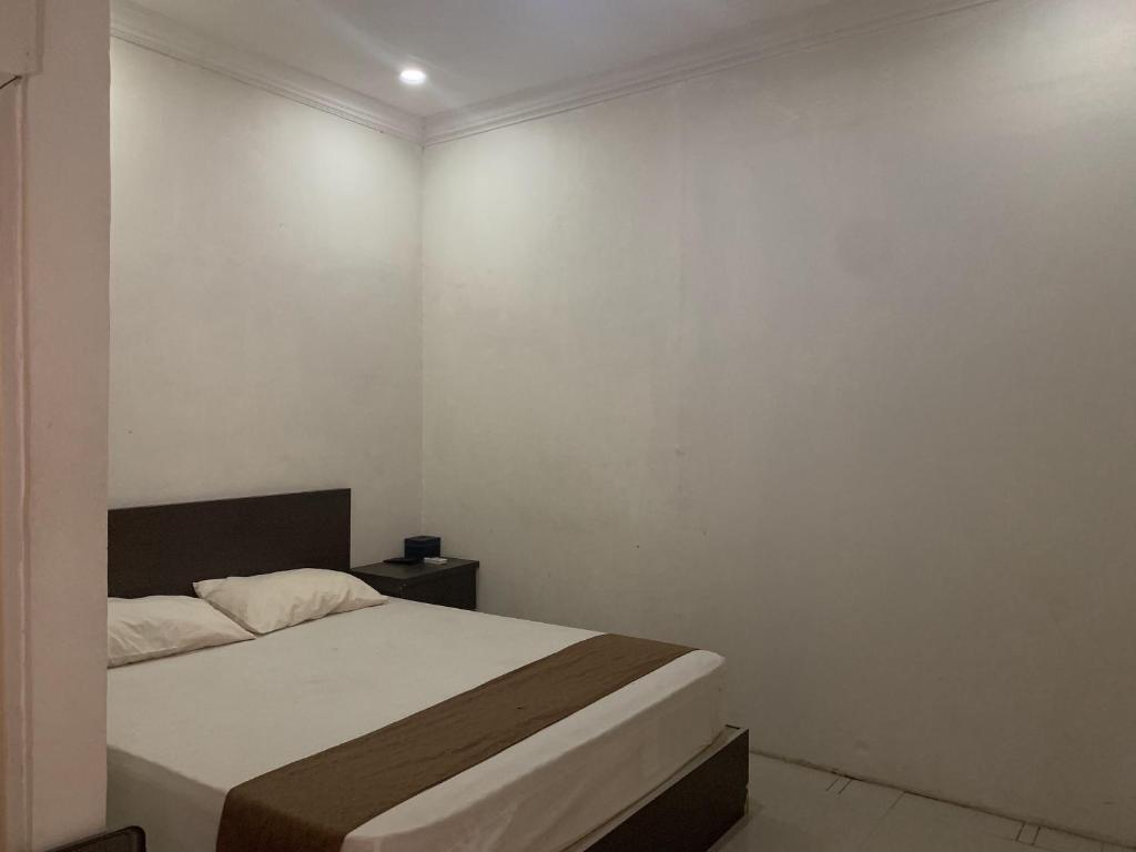 a bedroom with a bed and a white wall at Hotel O Penginapan Laota Syariah Near Rumah Sakit Islam Faisal Makassar in Luwuk