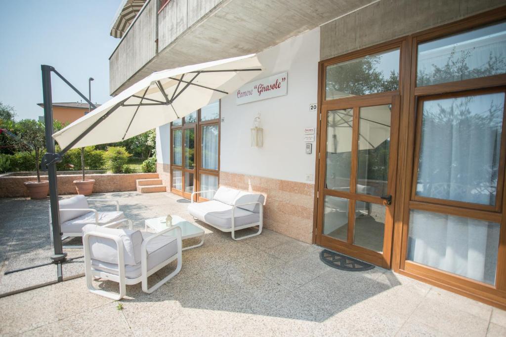 un patio con sillas blancas y una sombrilla en Camere Girasole, en Lazise