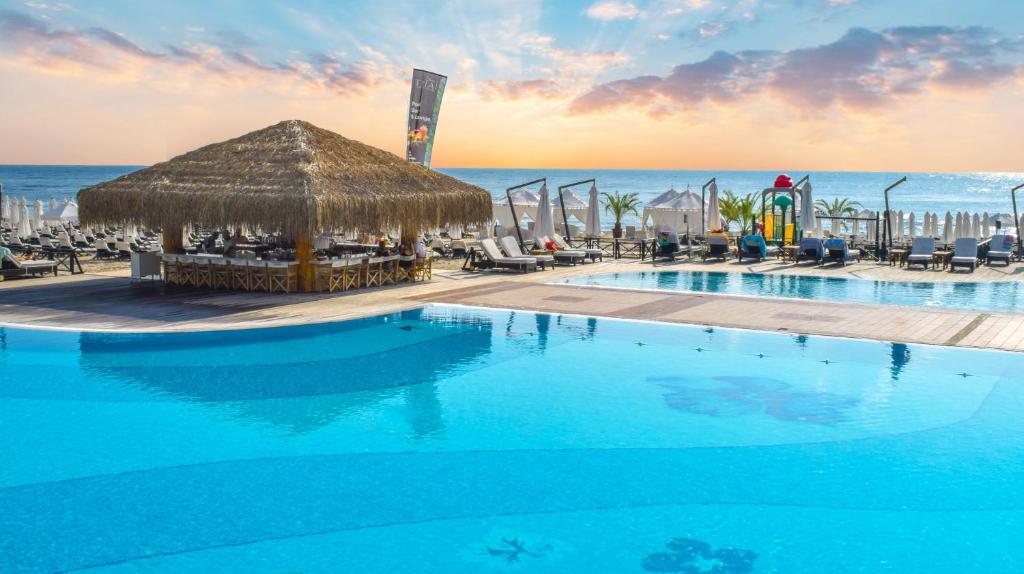 a large swimming pool with a thatch hut and the ocean at Oasis Resort Apartment, Луксозен Апартамент в комплекс ОАЗИС in Lozenets