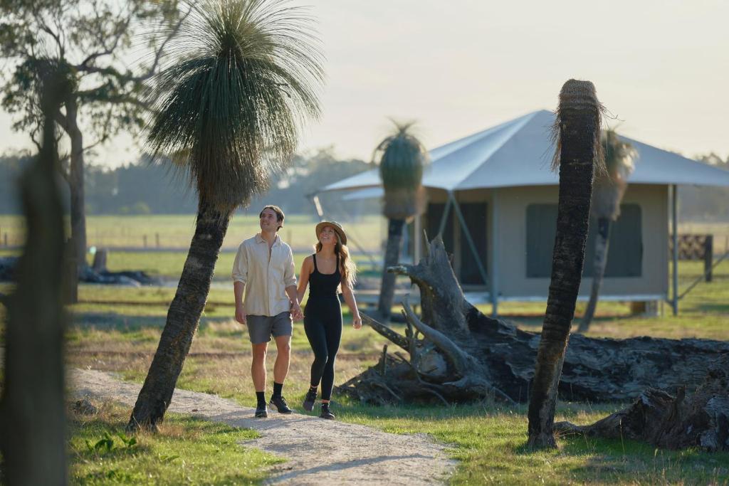 a man and woman walking down a path with palm trees at Willow Wood Glamping Retreat in Broadwater