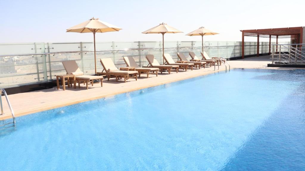 a swimming pool with chairs and umbrellas on a building at Al Riyadh Hotel Apartments in Abu Dhabi