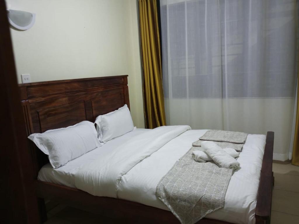 una camera da letto con letto, lenzuola e cuscini bianchi di Lux Suites Wawazi Court Apartments a Nairobi