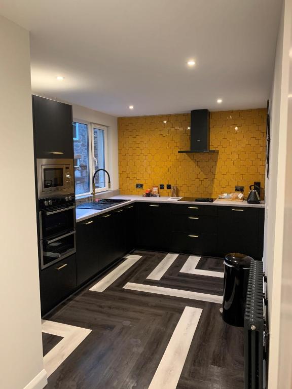 a kitchen with black cabinets and yellow tiles at Hillview in Oban