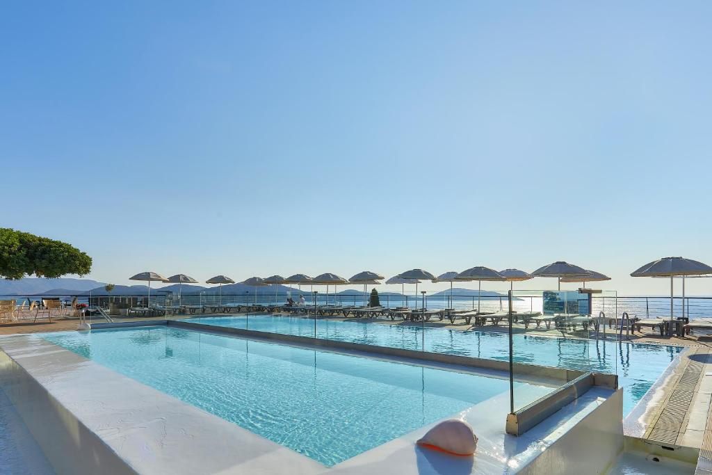 a large swimming pool with tables and umbrellas at Elounda Ilion Hotel Bungalows in Elounda