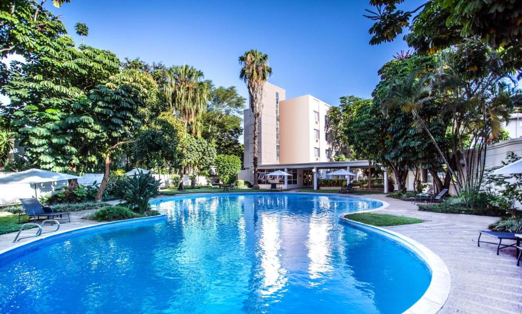 a swimming pool with palm trees and a building at Southern Sun Ridgeway Lusaka in Lusaka