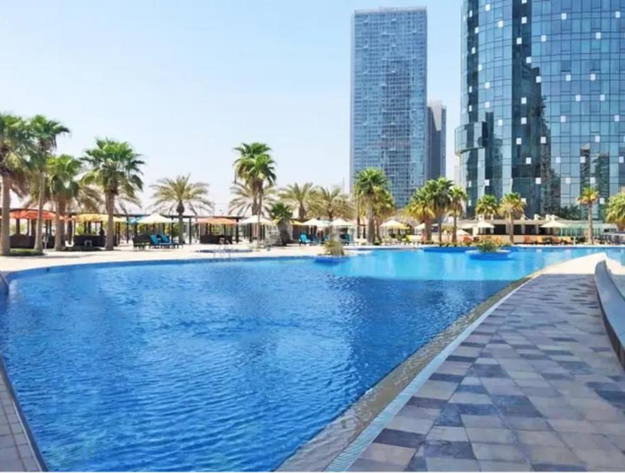 a large swimming pool with palm trees and buildings at Casa Su Casa in the Sky 5906 in Abu Dhabi