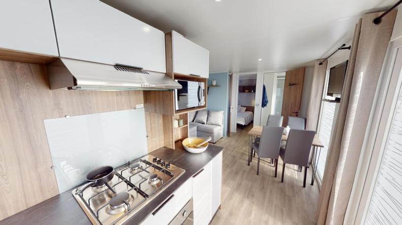 a kitchen with a stove top oven next to a living room at Mobil home 4&#47;6 personnes in Seignosse