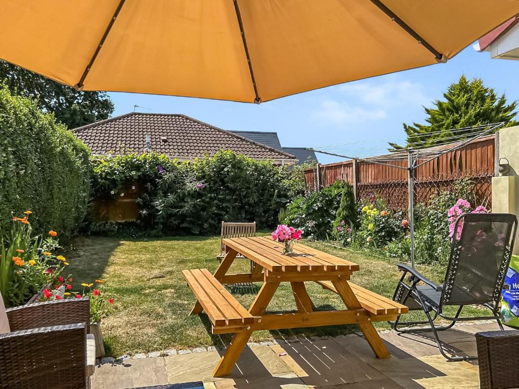 a wooden picnic table in a yard with an umbrella at Selsmore Cottages in South Hayling
