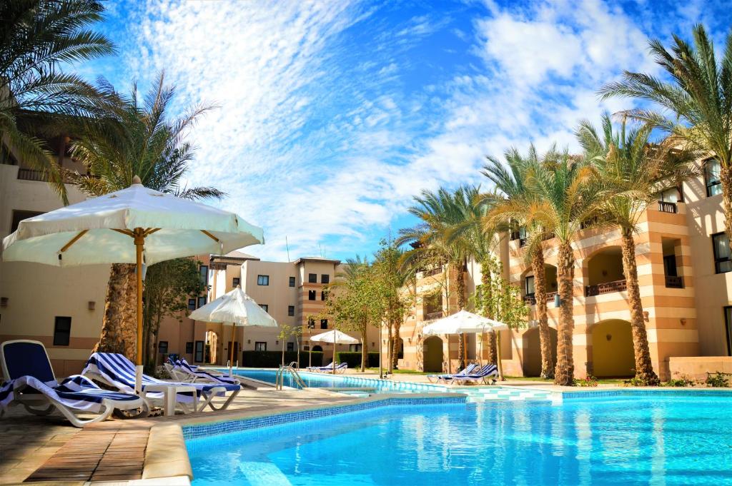 una piscina con sillas, sombrillas y palmeras en Port Ghalib Marina Residence Suites, en Port Ghalib