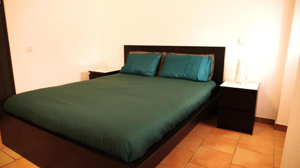 a bedroom with a bed with green sheets and blue pillows at Casa na Vila T2 in Fuzeta