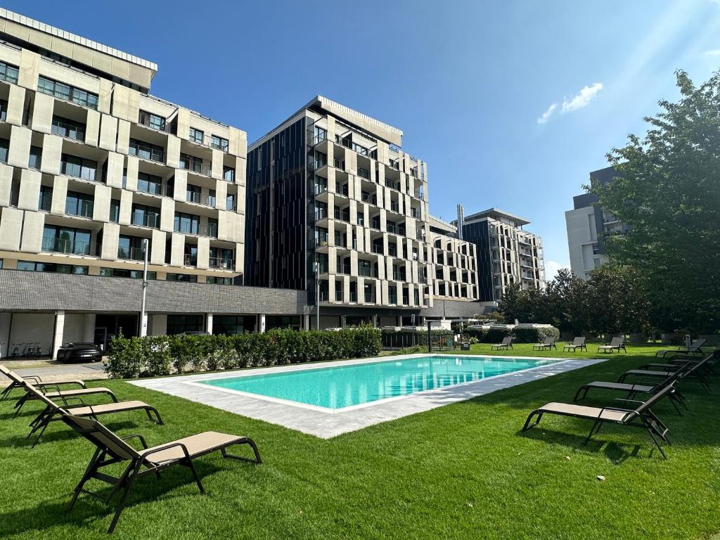 a swimming pool in a park with benches and buildings at Ramada Plaza Milano in Milan